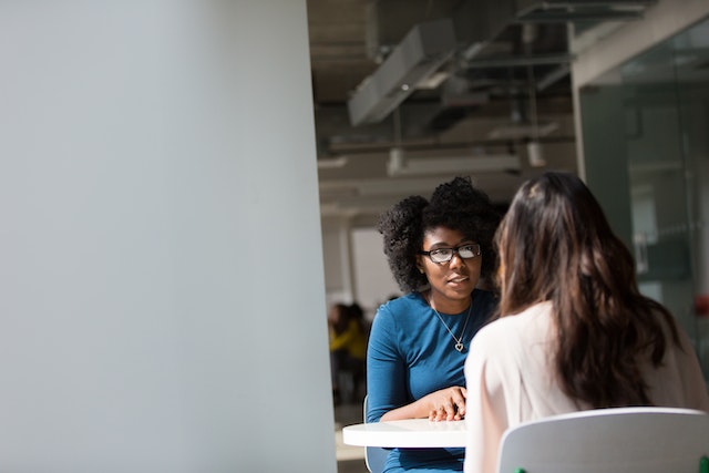 person in a blue shirt speaking to someone in a white shirt white seated at an office table